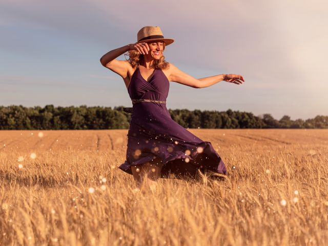 Mujer bailando sonriente en un campo de trigo - vivir mal es lo normal